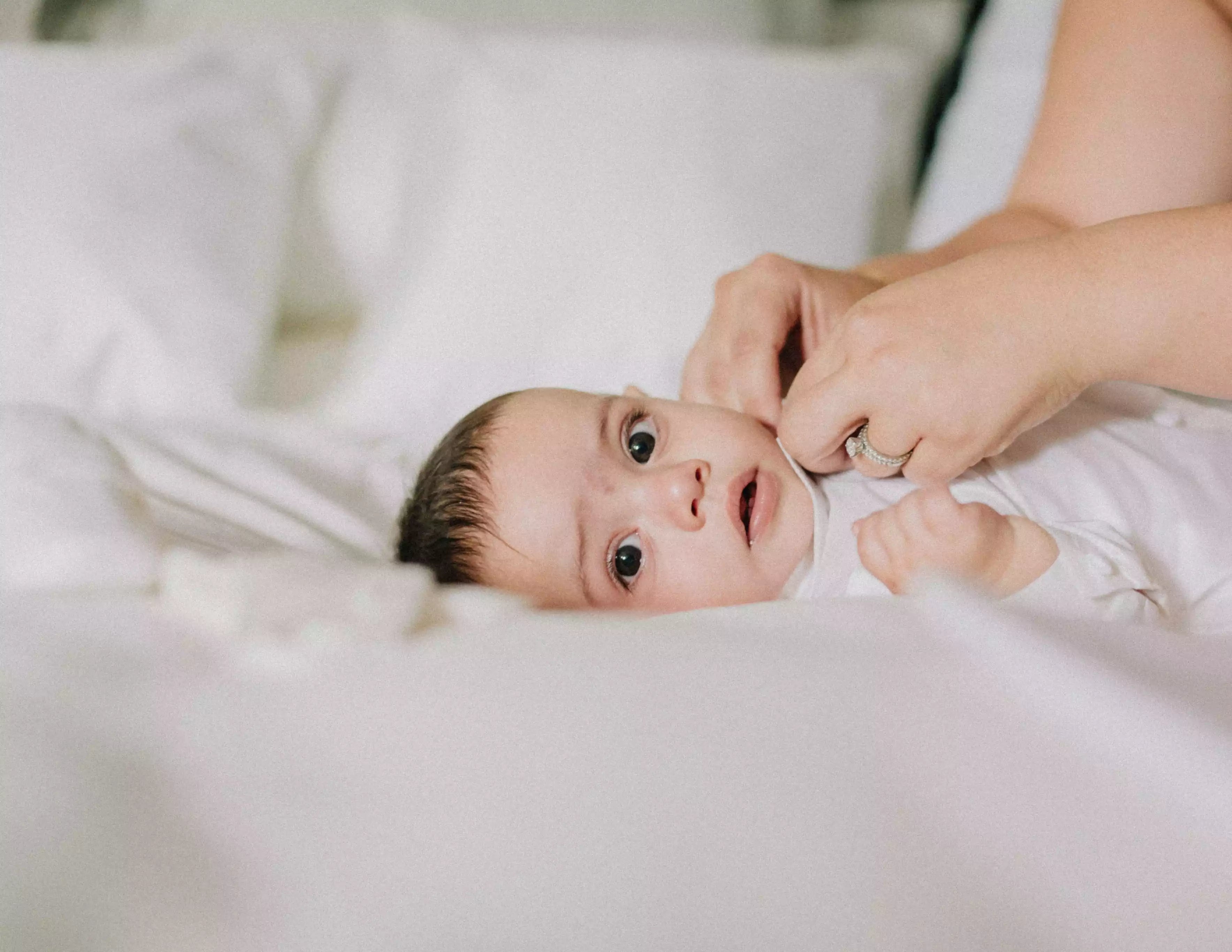 Baby das auf einem weißen Bett liegt und in die Kamera schaut