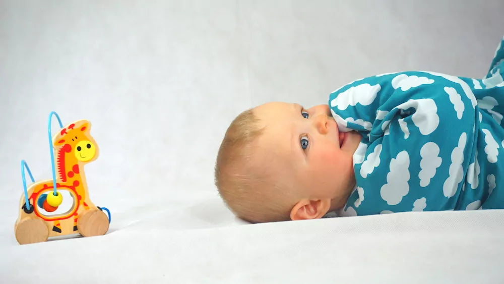 Baby liegt neben einem Kinderspielzeug auf dem Rücken und schaut in die Ferne